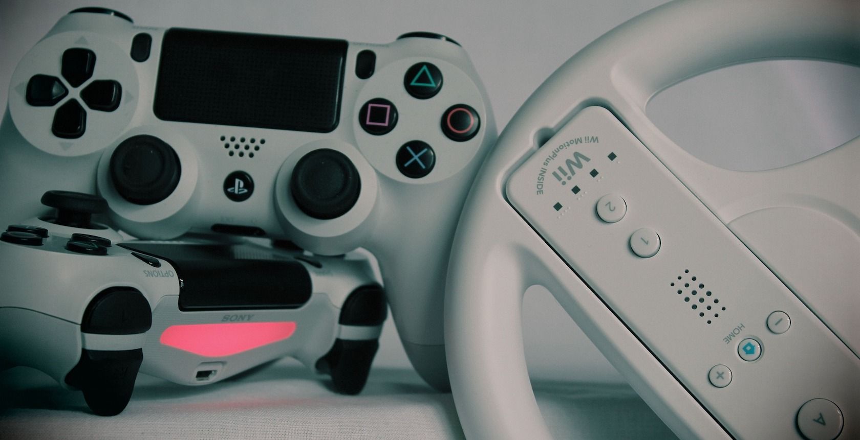 A photograph of two PlayStation 4 controllers and a Wii controller in a steering wheel accessory