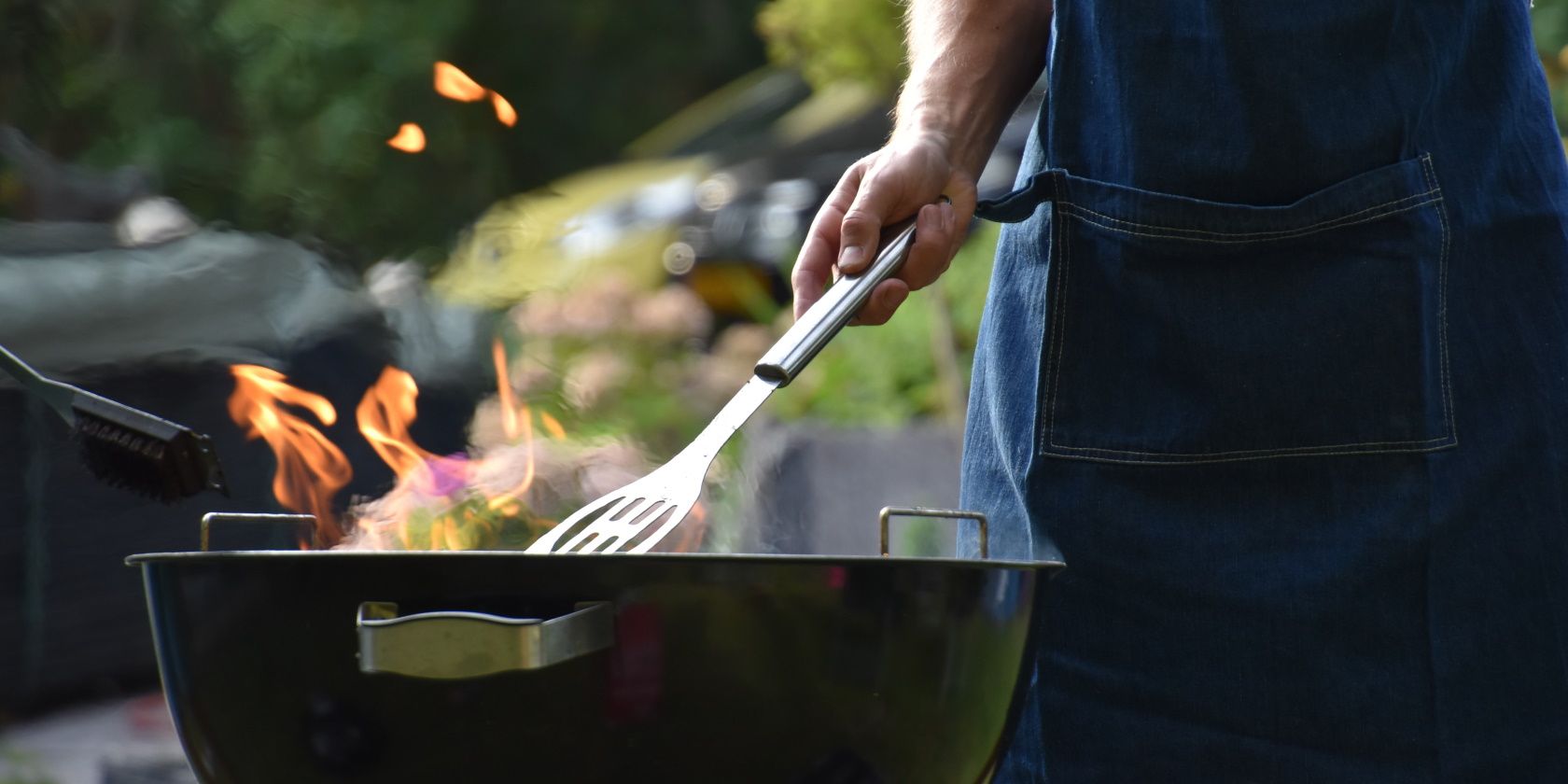 Person in denim apron cooking on a kettle grill