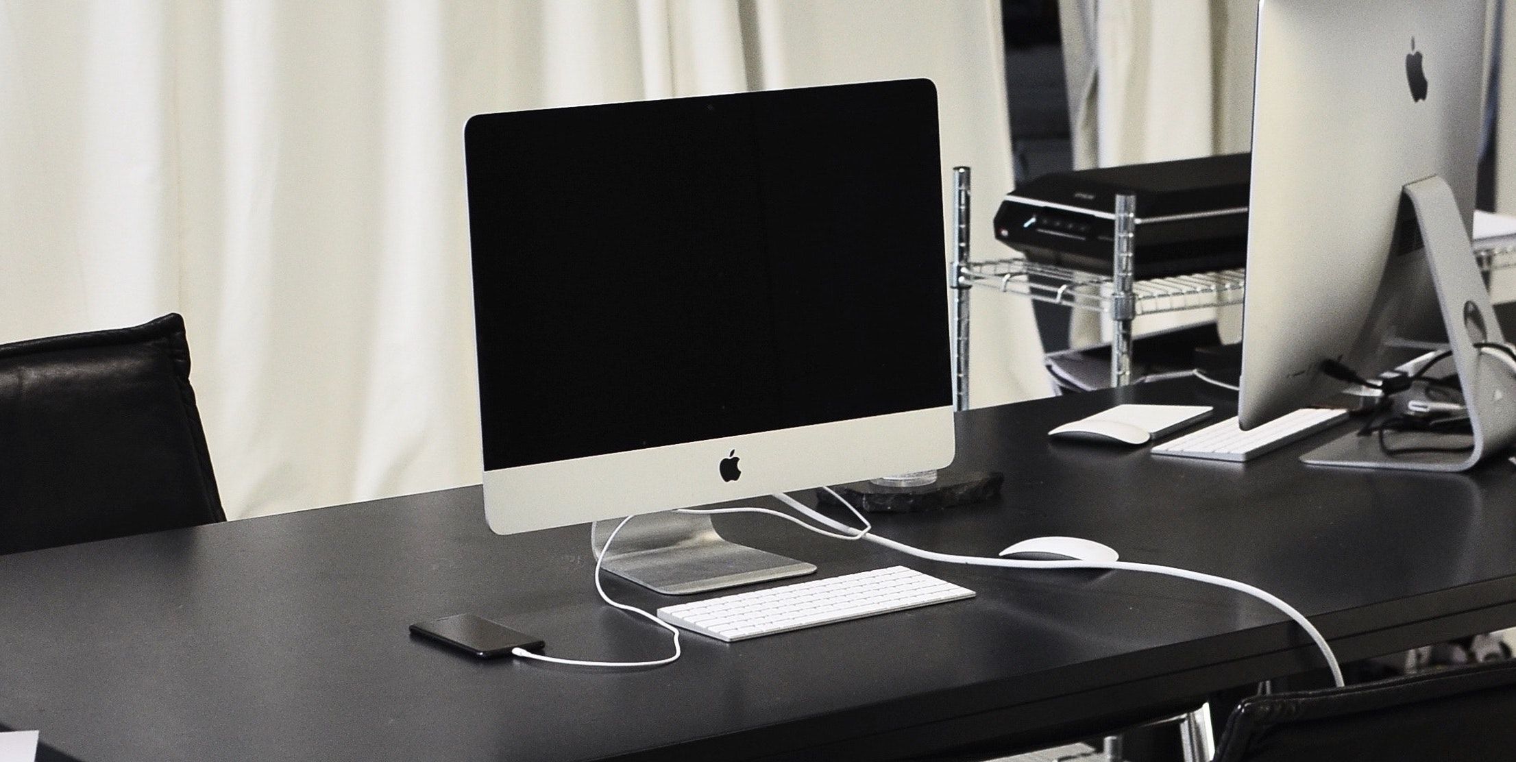 An iPhone charges beside an iMac on a desk
