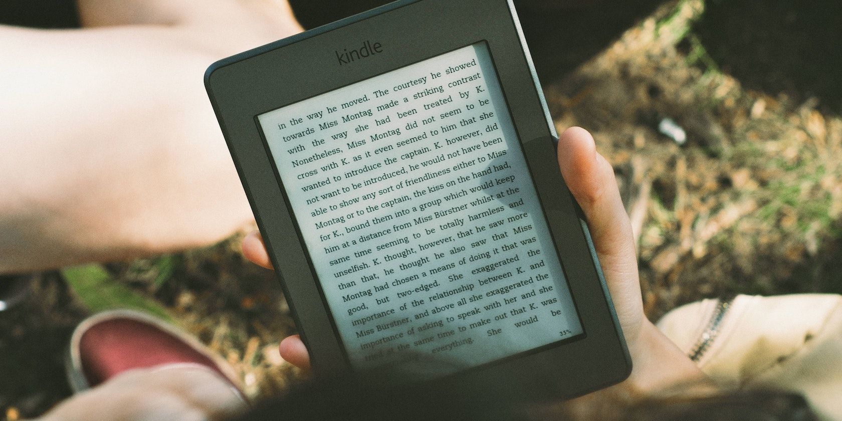 A person reading a Kindle outdoors.