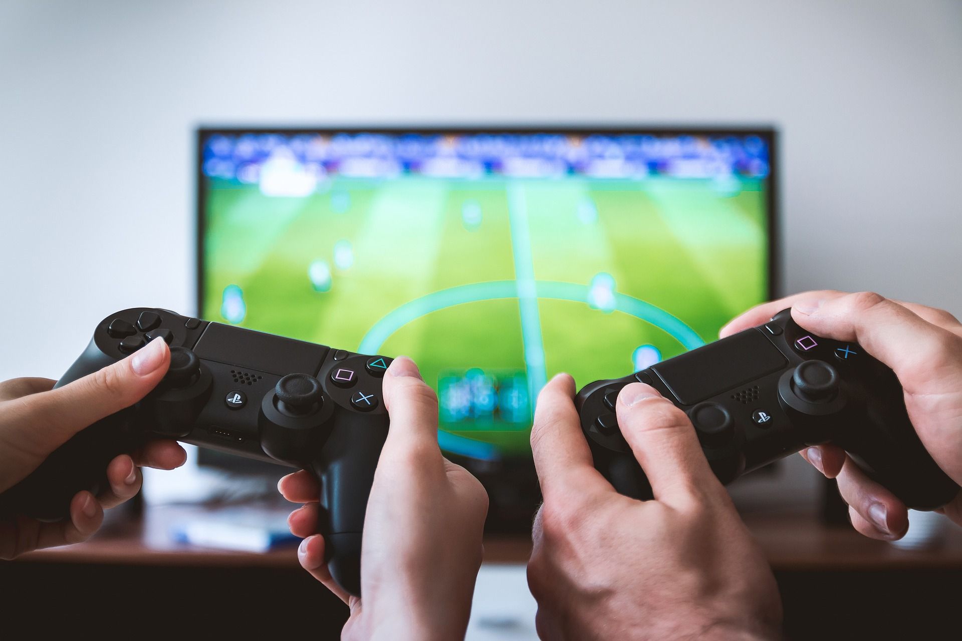 two hands holding video game controllers with television in background