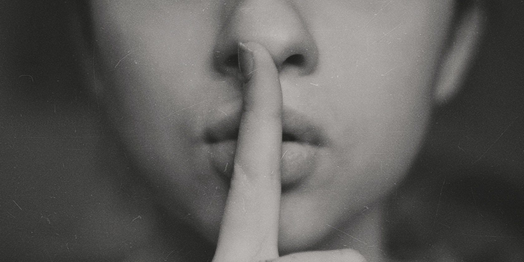 A photograph of someone holding their index finger up to their lips in a shushing motion