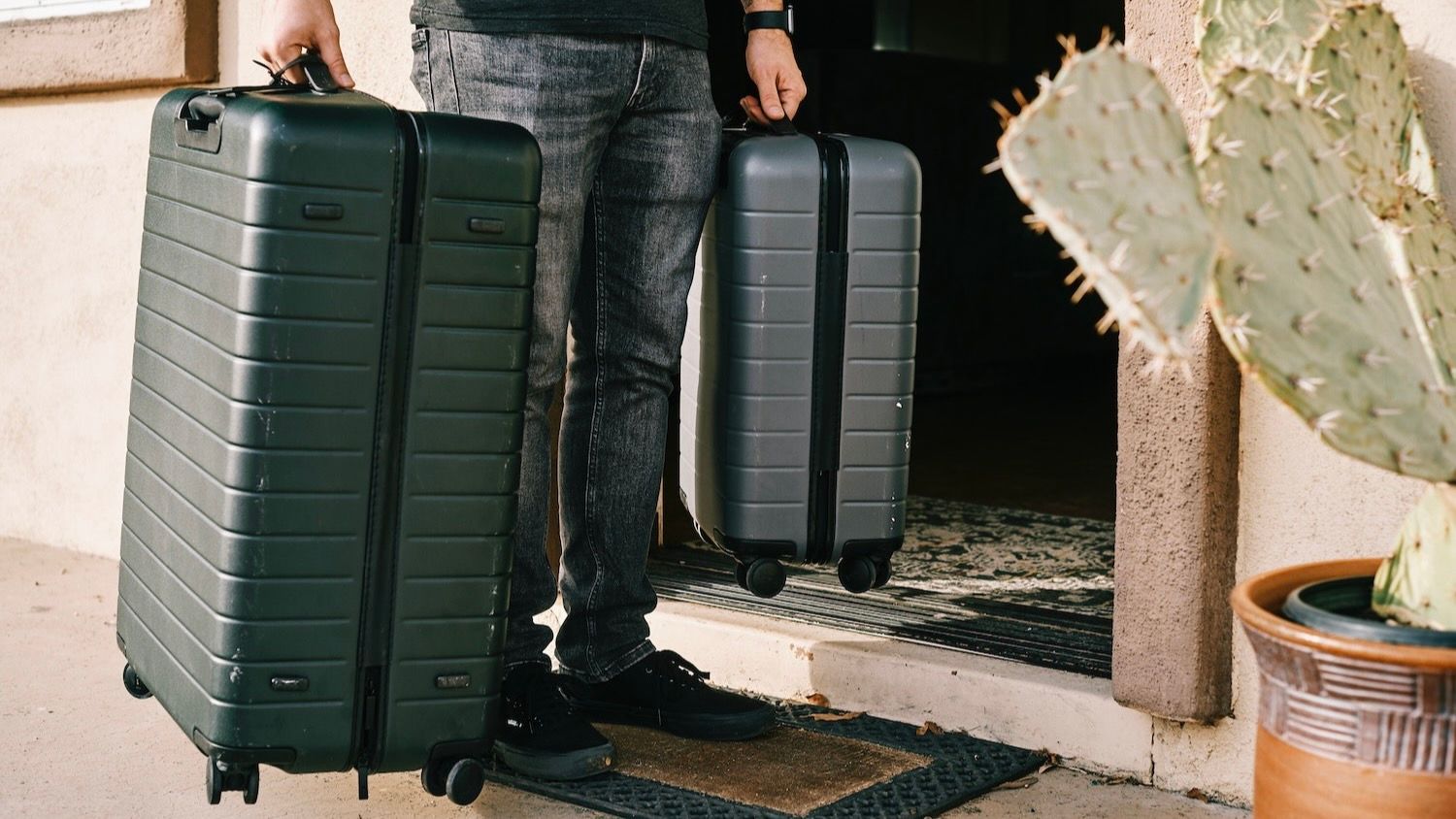 Person carrying two hard suitcases in front of door