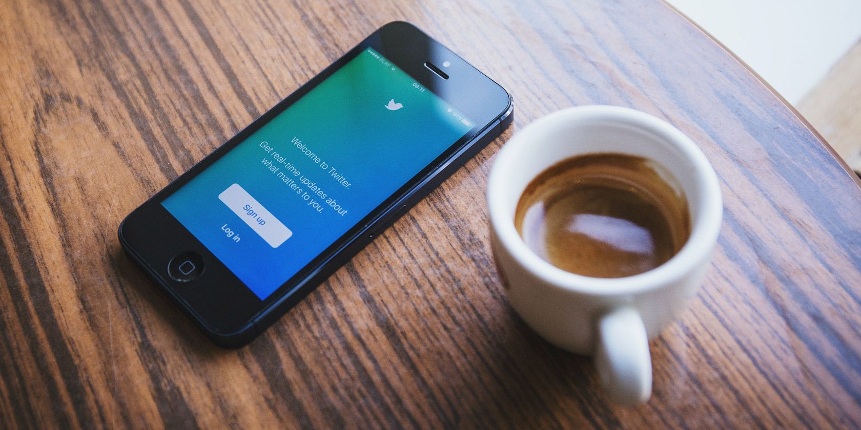 Twitter open on a mobile phone next to a coffee mug