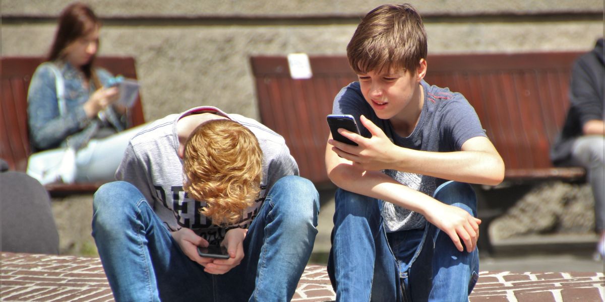 Two boys sitting on a wall with cellphones