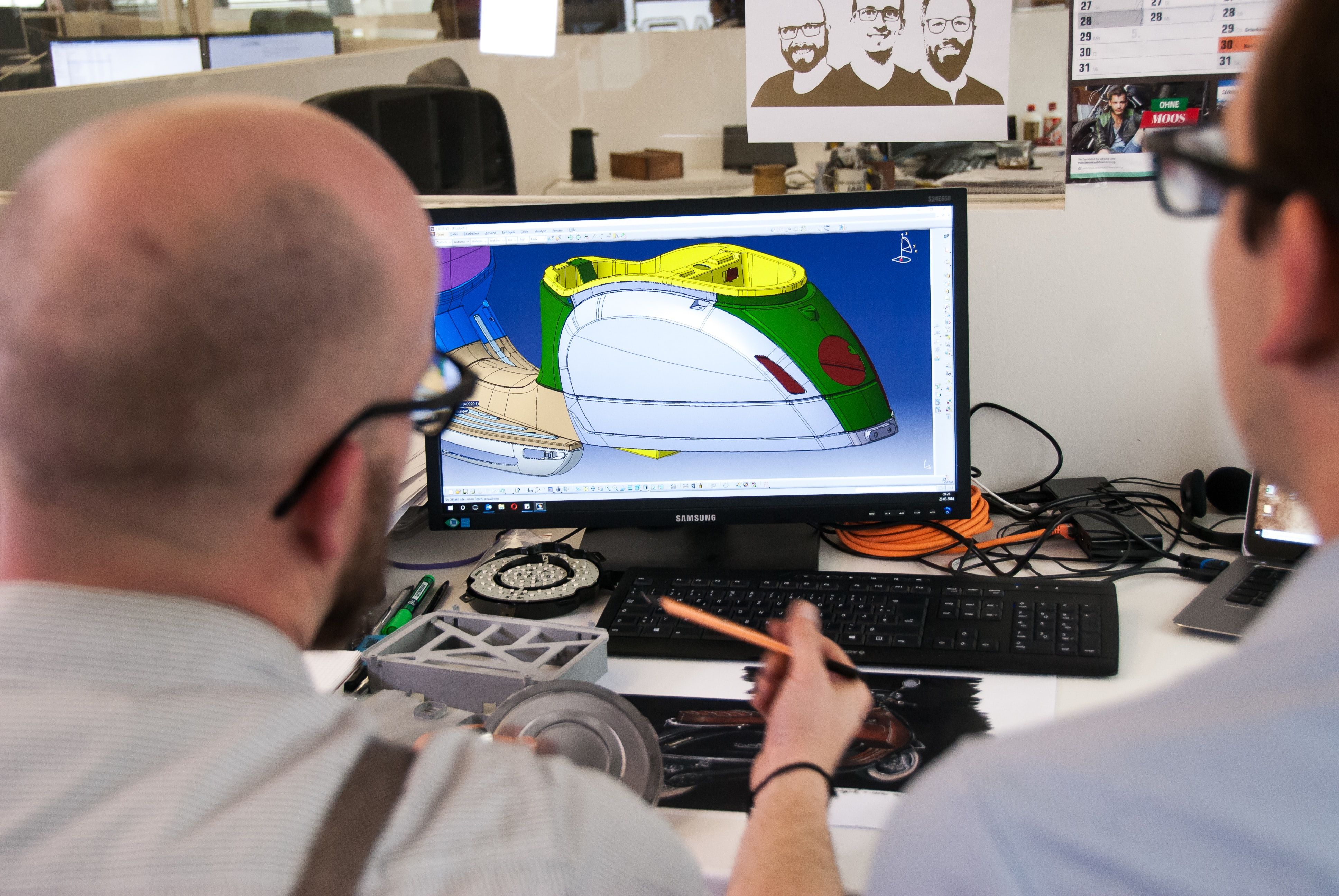 Two men sitting together, collaborating on the design of a 3D object on CAD software