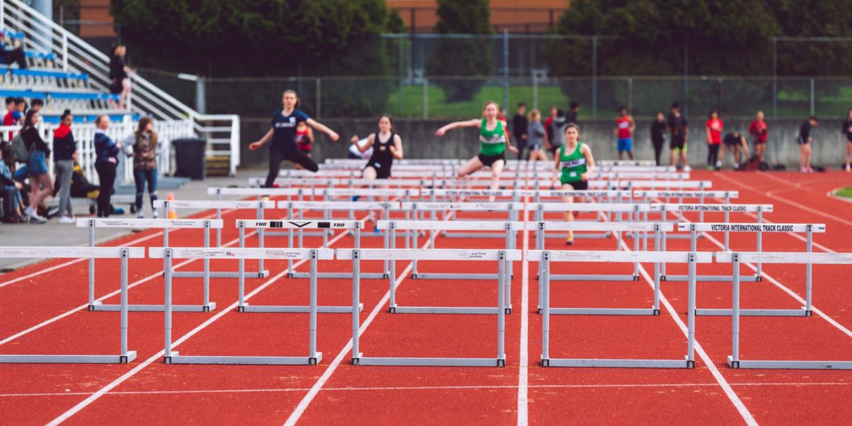 Athletes running on track with hurdles