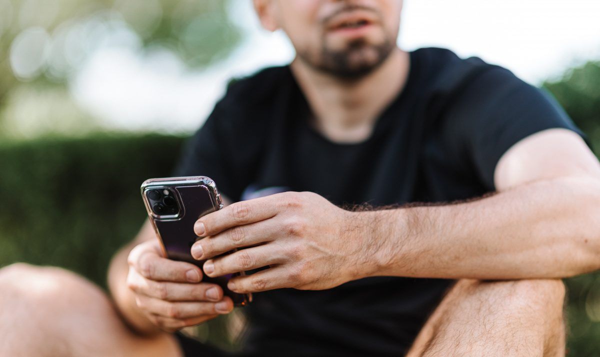 Homem sentado na grama com um celular na mão