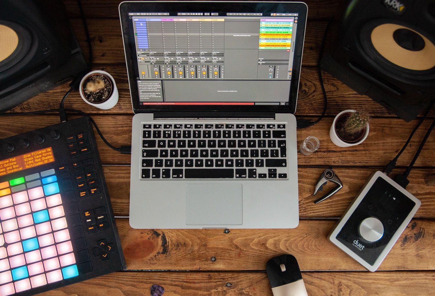 A photo of a Macbook device on a desk, with the Ableton Live DAW open, together with an Ableton Push and Audio Interface
