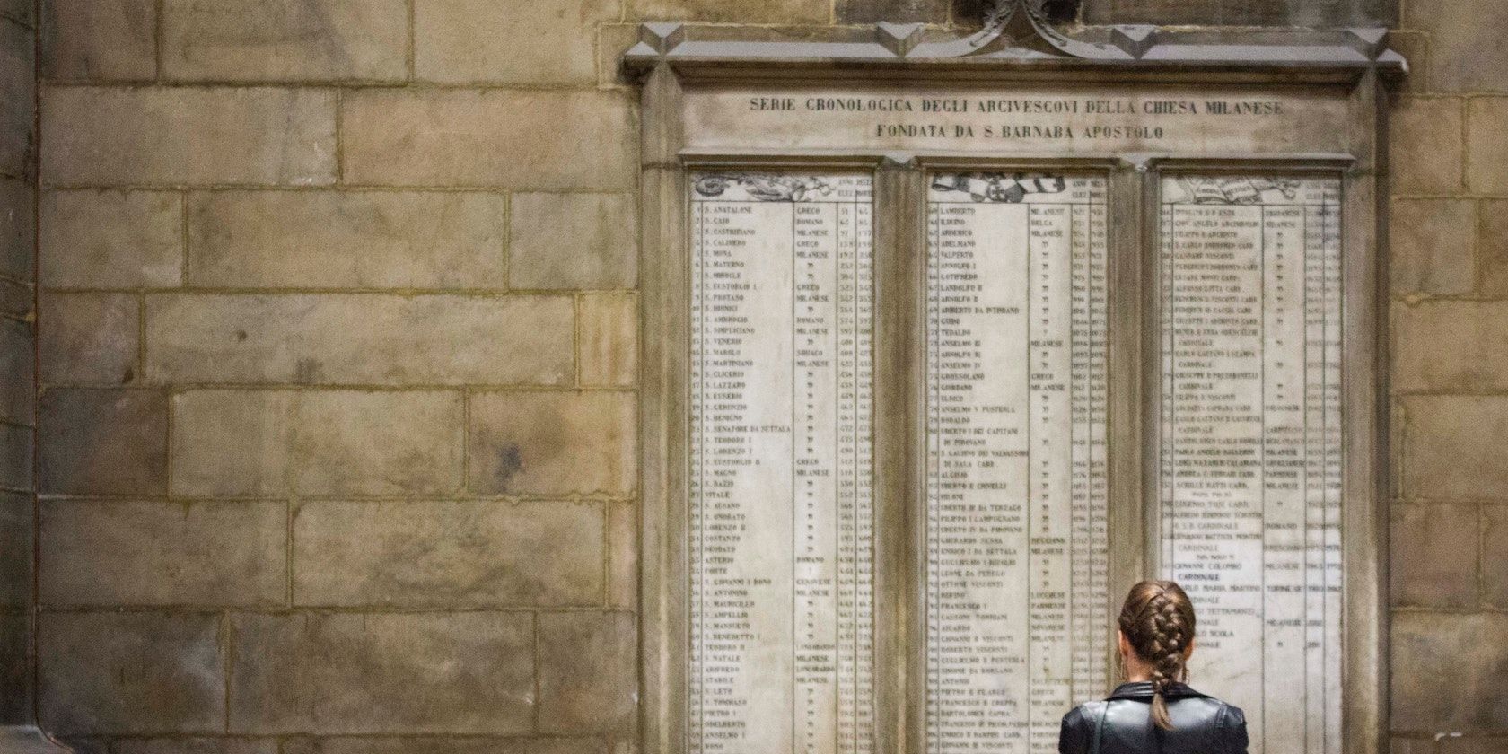 A photograph of somebody looking away from the camera, at a long list of names carved in stone