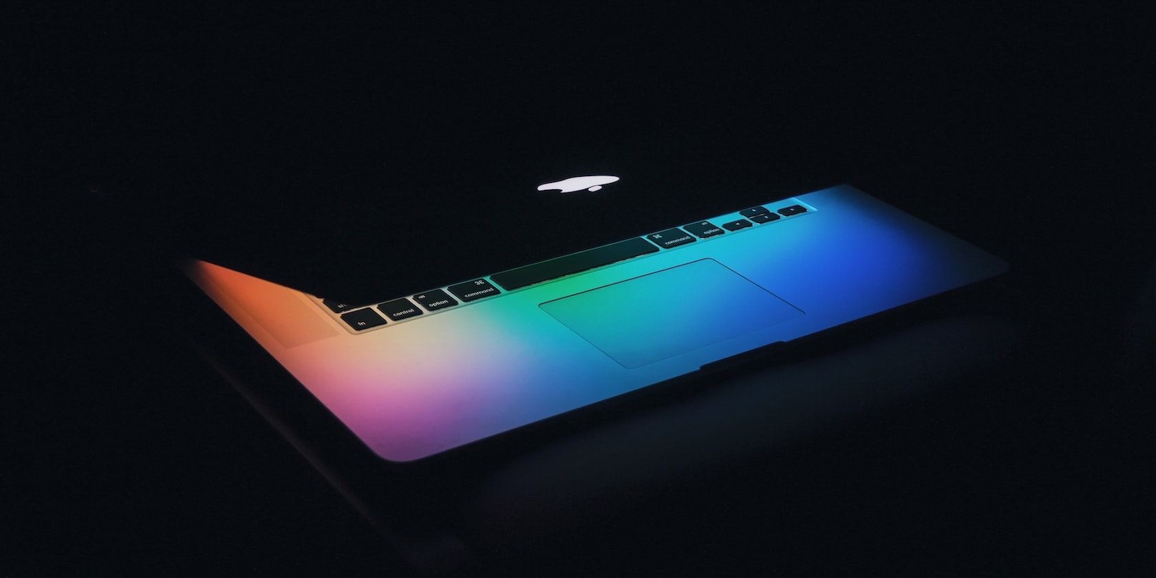 A photo of an Apple Mac computer with its lid partially closed, with a colorful desktop background
