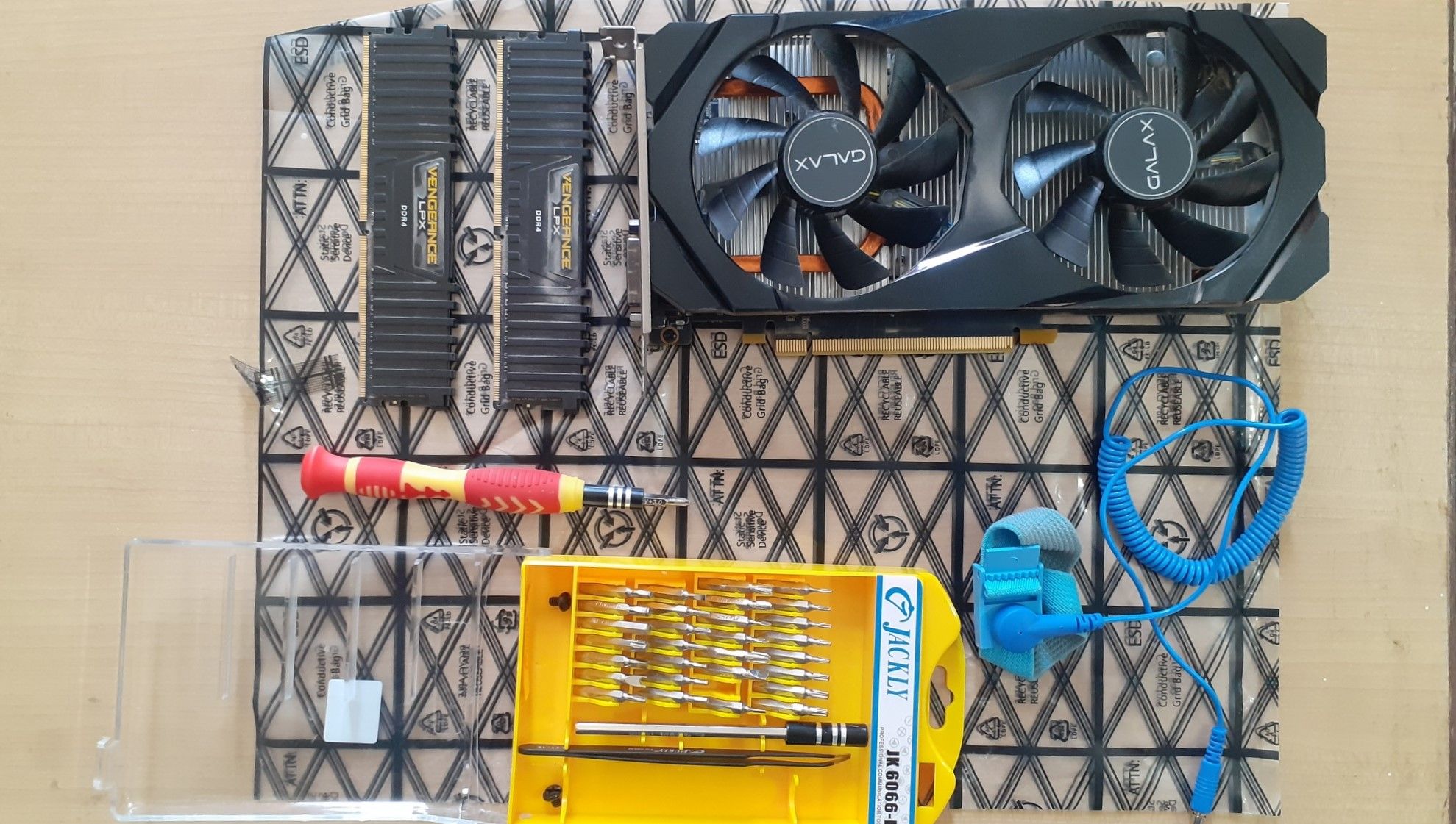 A GPU, RAM sticks, screwdriver kit, and an antistatic wristband lying on a motherboard sleeve.
