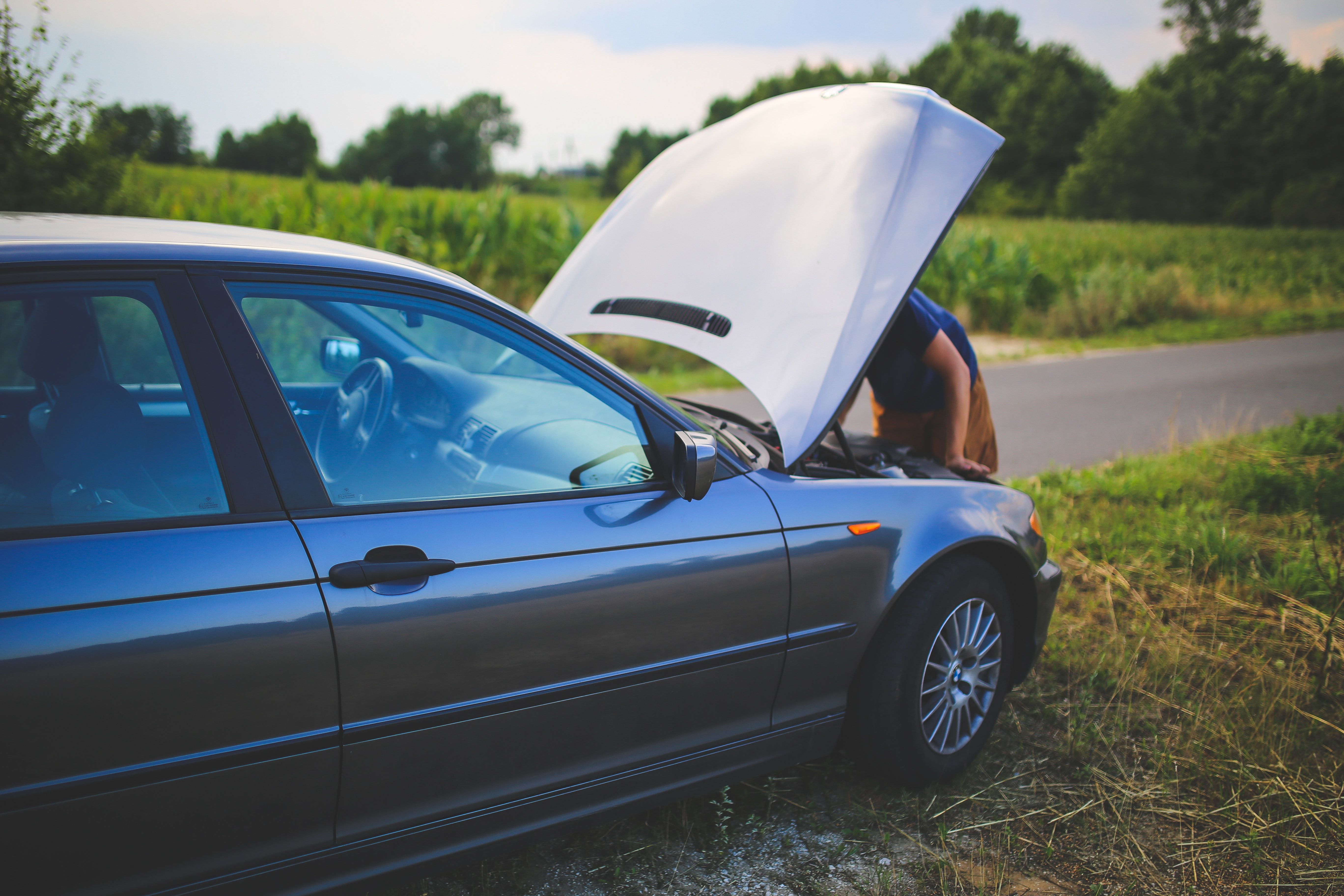 Person checking under the hood of a car on side of the road