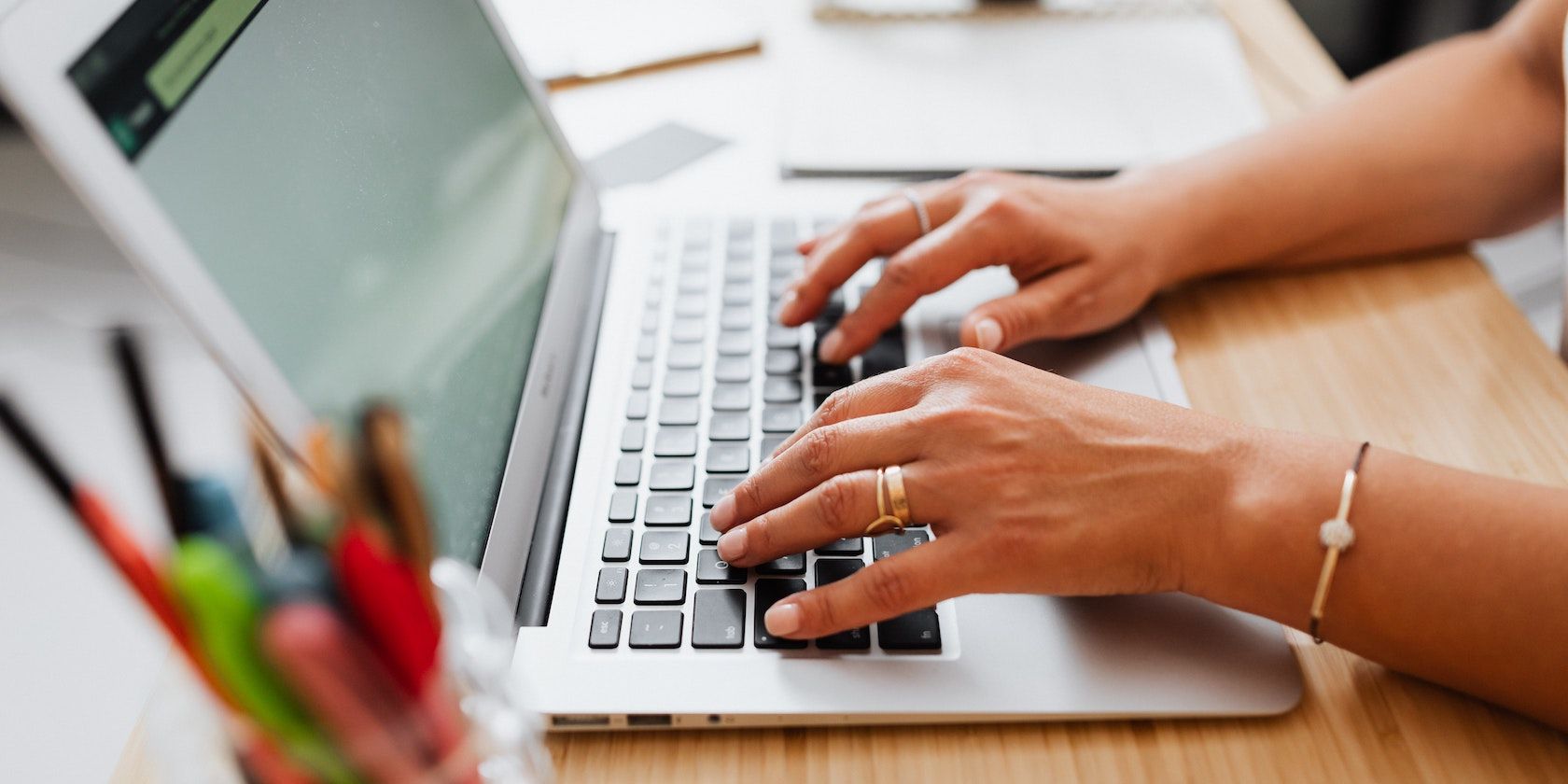 A person types on a MacBook keyboard while the MacBook sits on a desk