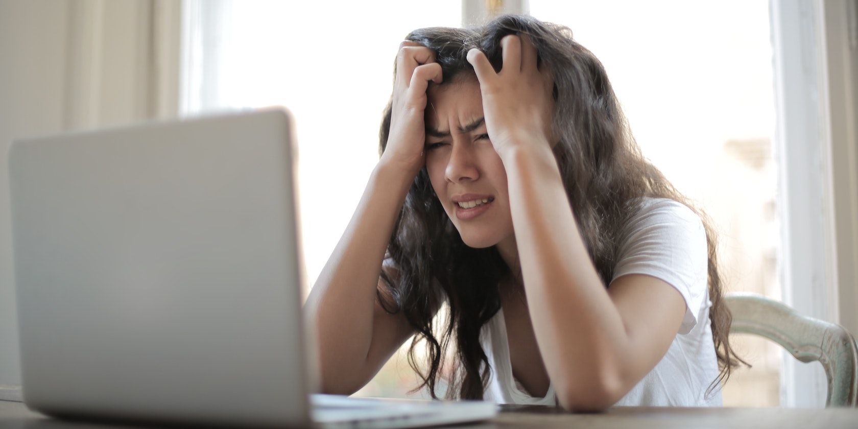 Woman grabs her hair in frustration while looking at a laptop