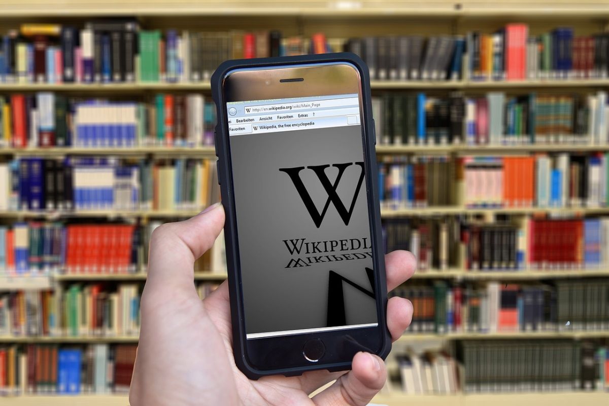 A smartphone in a hand with books in the background