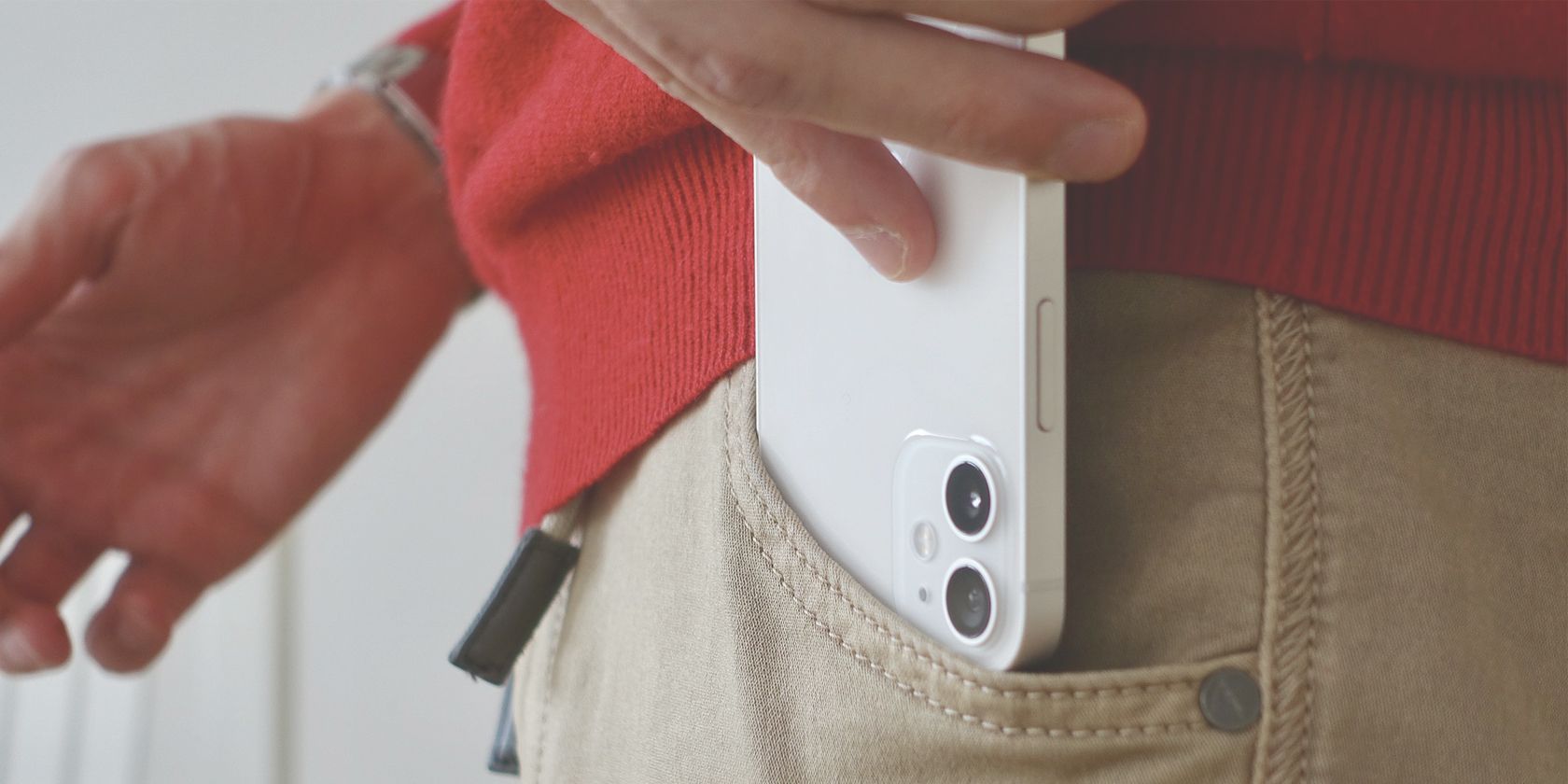 Close up of a white iPhone 12 mini being put into a pocket on a pair of brown jeans. 