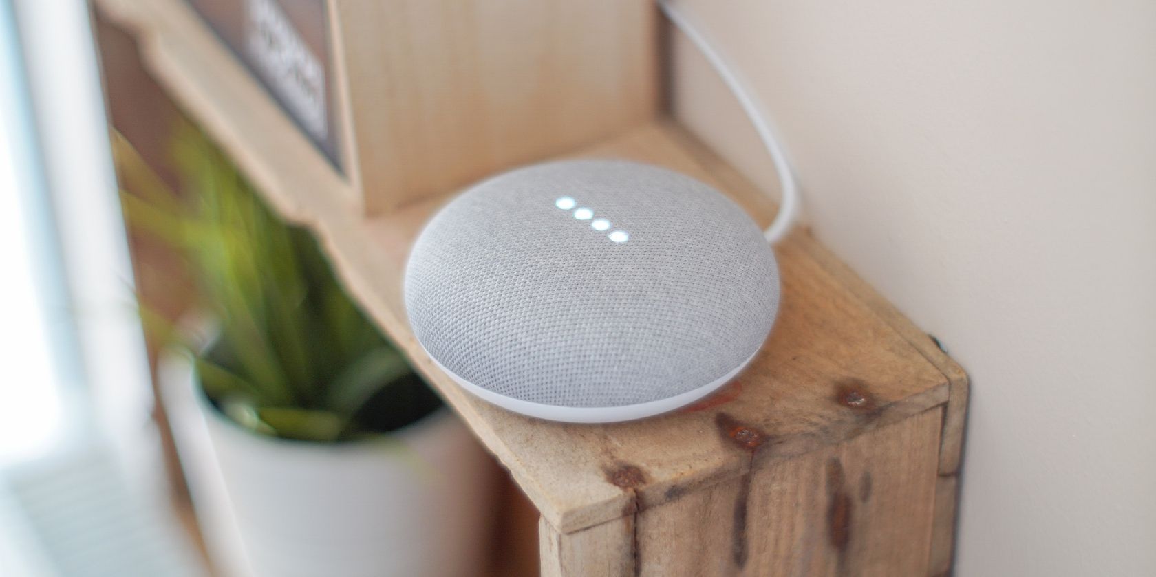 Gray Google Home Mini Speaker sitting on wooden shelf