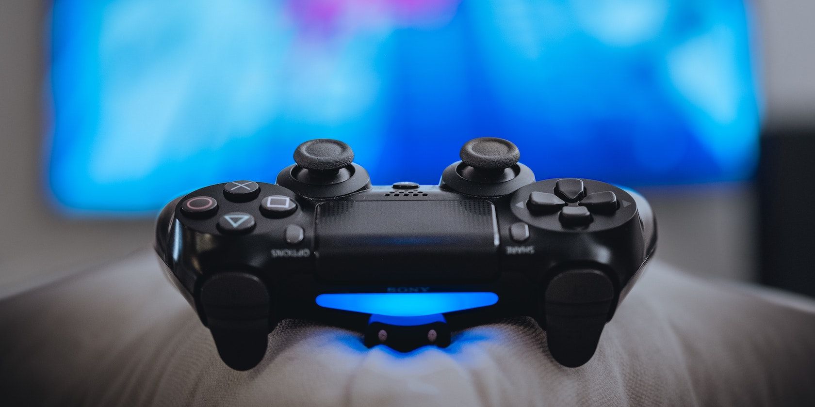 A black PS4 controller facing the camera emitting a blue light