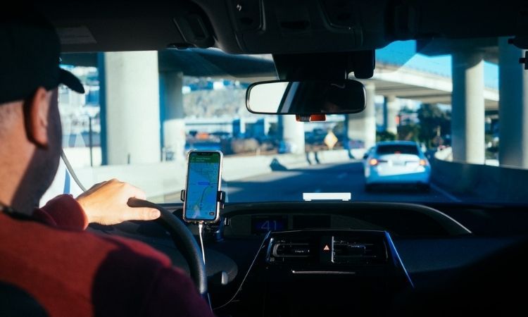 man in car driving with maps app on phone