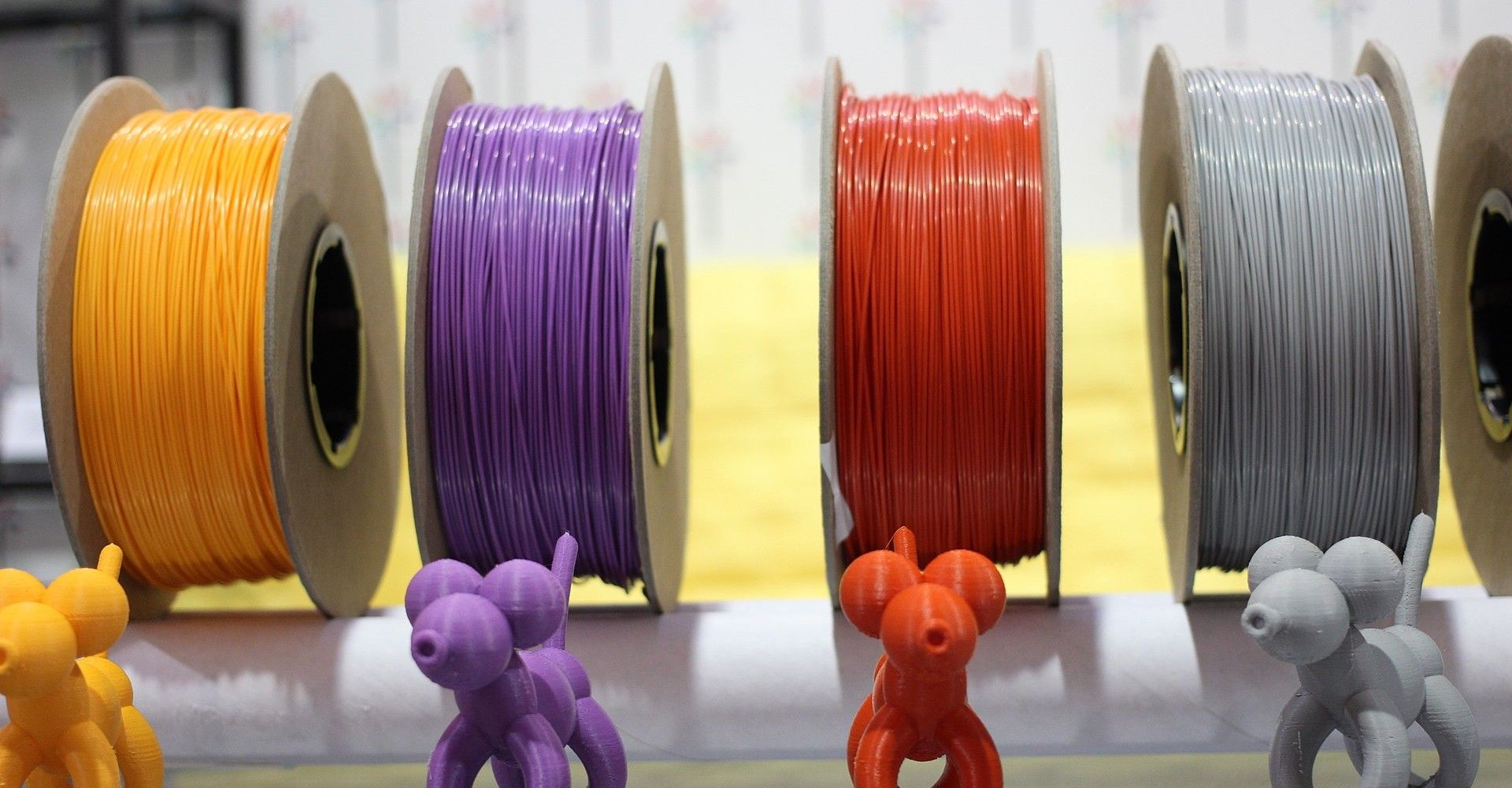 Four spools of 3D printing filament material in yellow, purple, orange and gray
