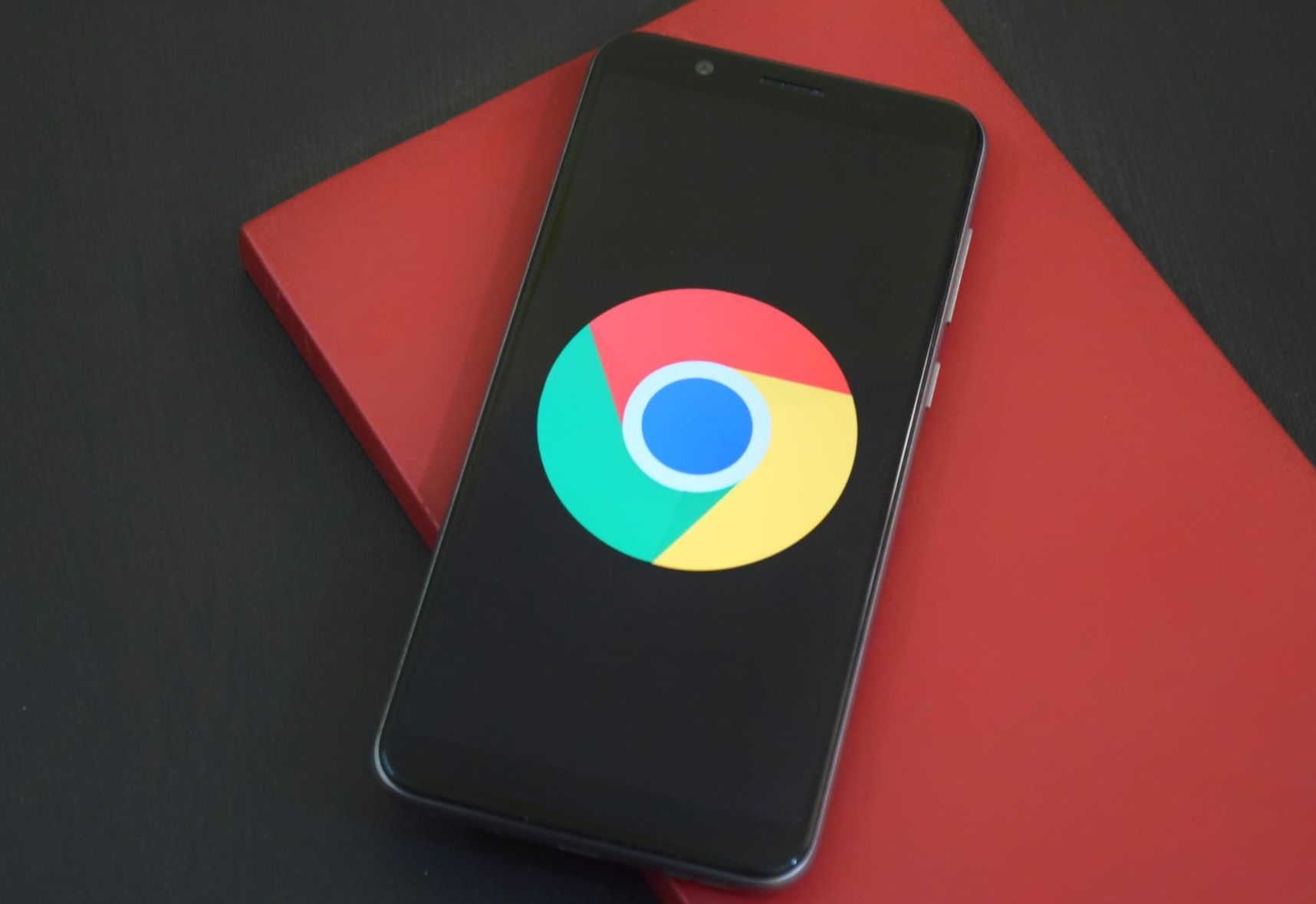 The Google Chrome icon on a black phone resting on a red surface