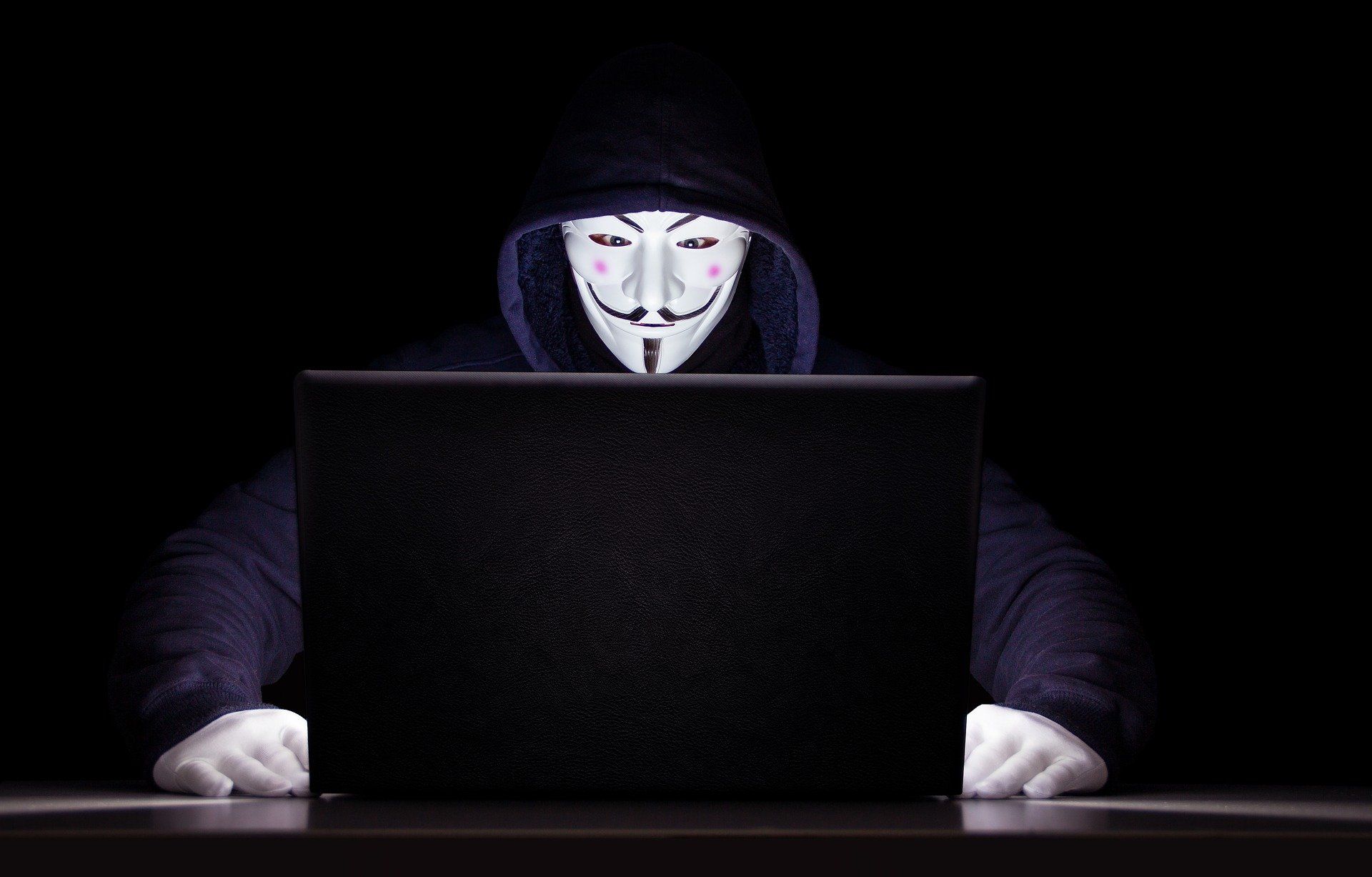 Person wearing anonymous mask sitting at the computer 