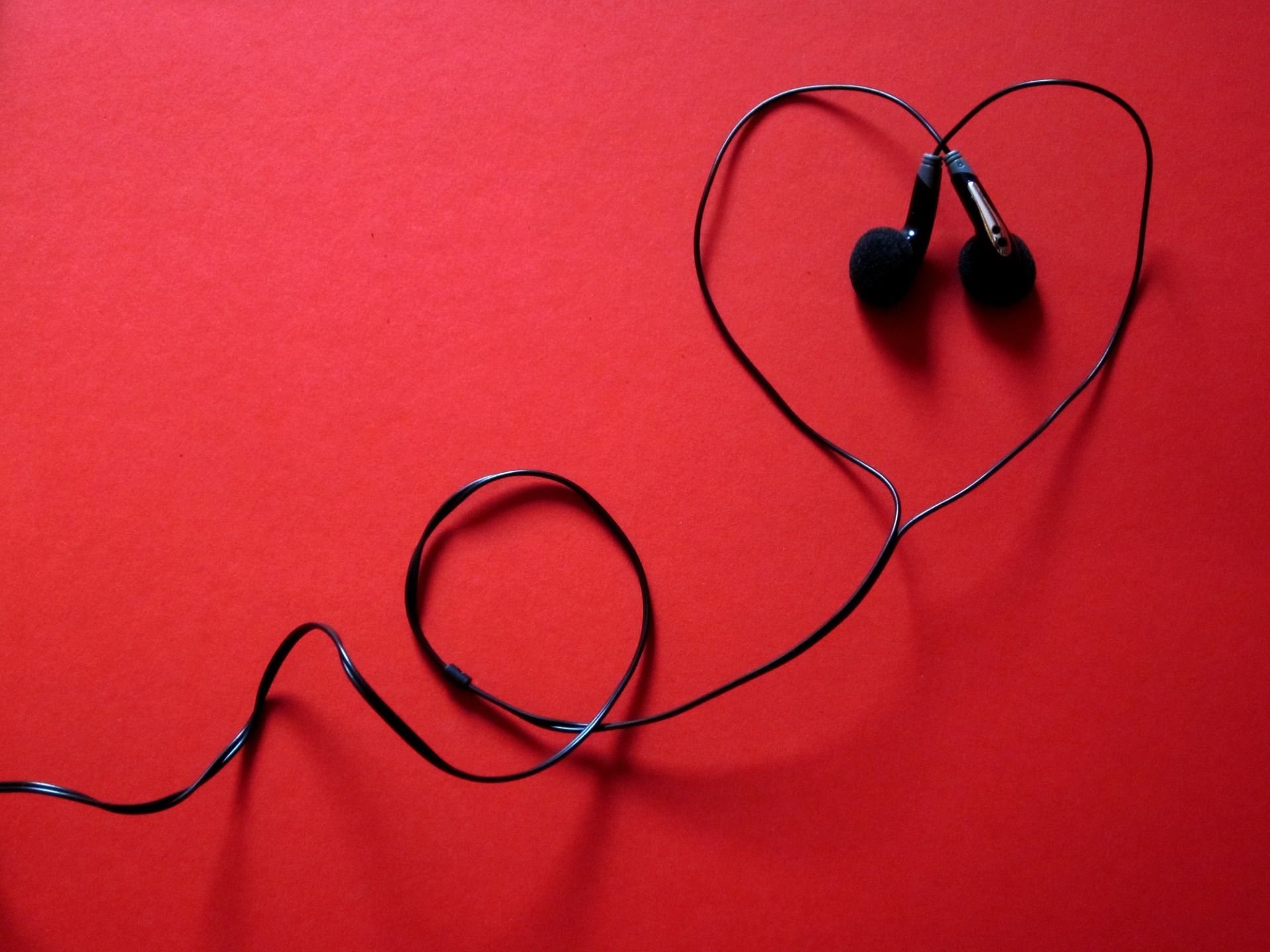 black earbuds in shape of heart on red background