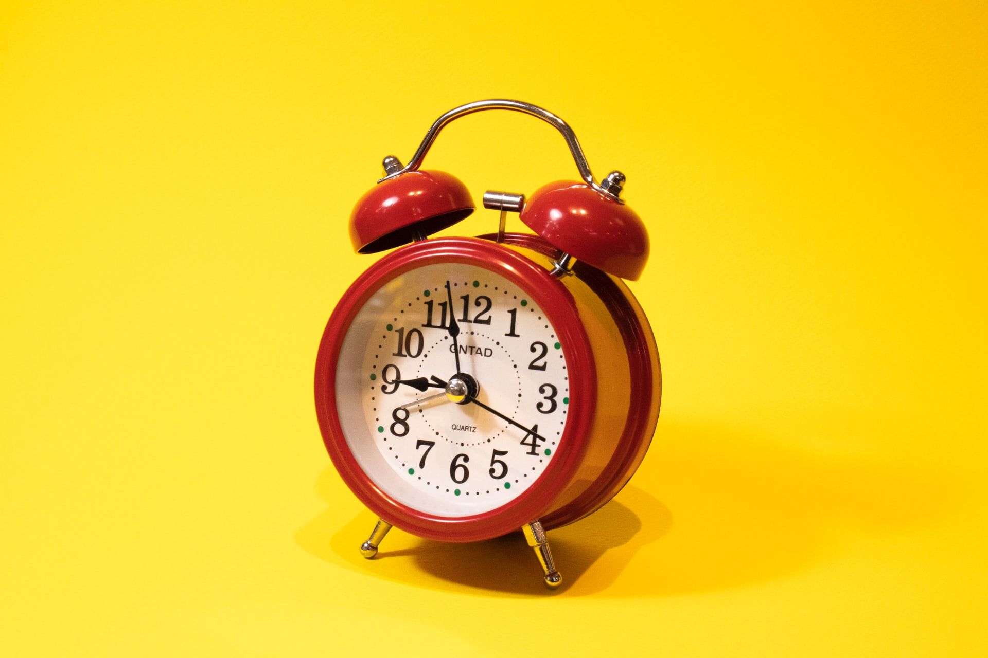 Image shows a bright red alarm clock on a yellow background