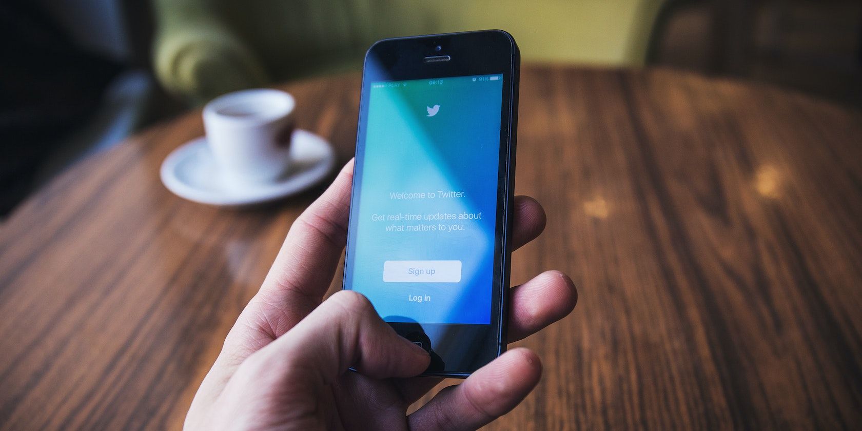 A hand holding a mobile phone which shows the twitter welcome screen