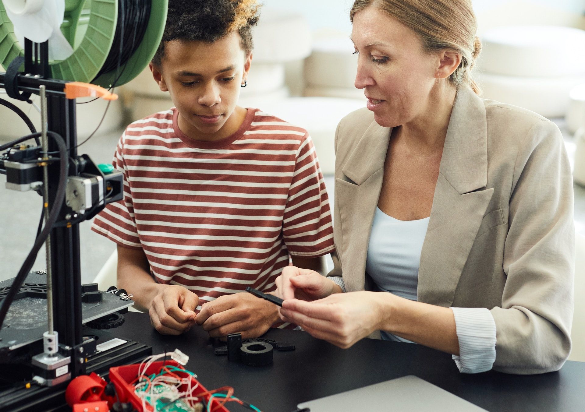 A woman sitting next to a boy showing him 3D printing parts