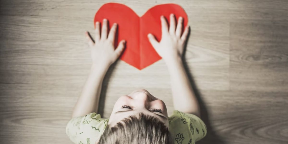 boy's hands touching red paper heart cutout on wooden floor