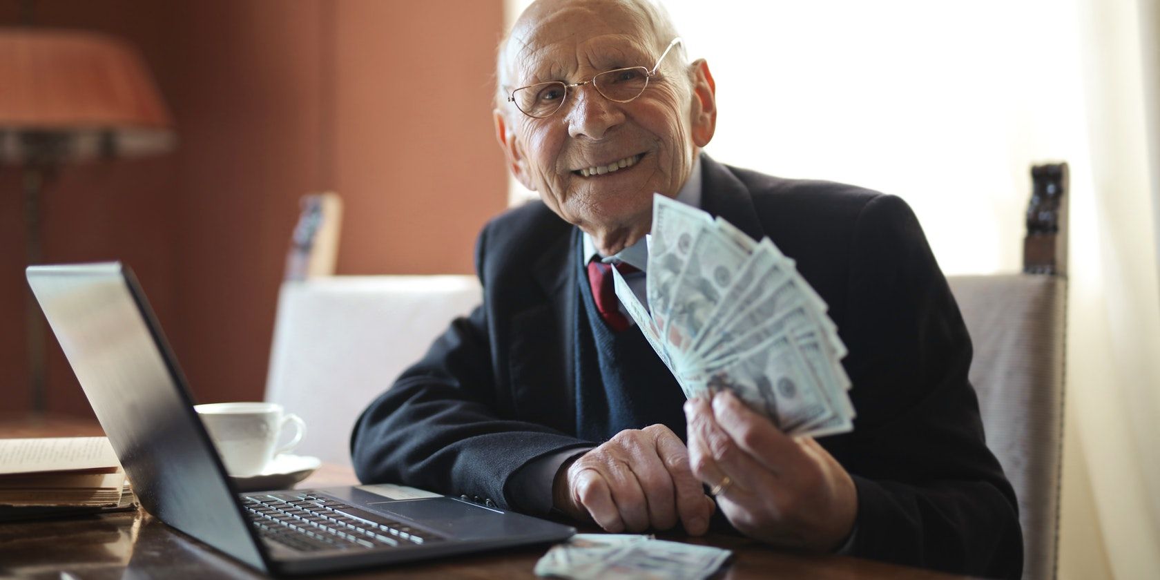 Photo of a man holding money in his hand Next to a Laptop