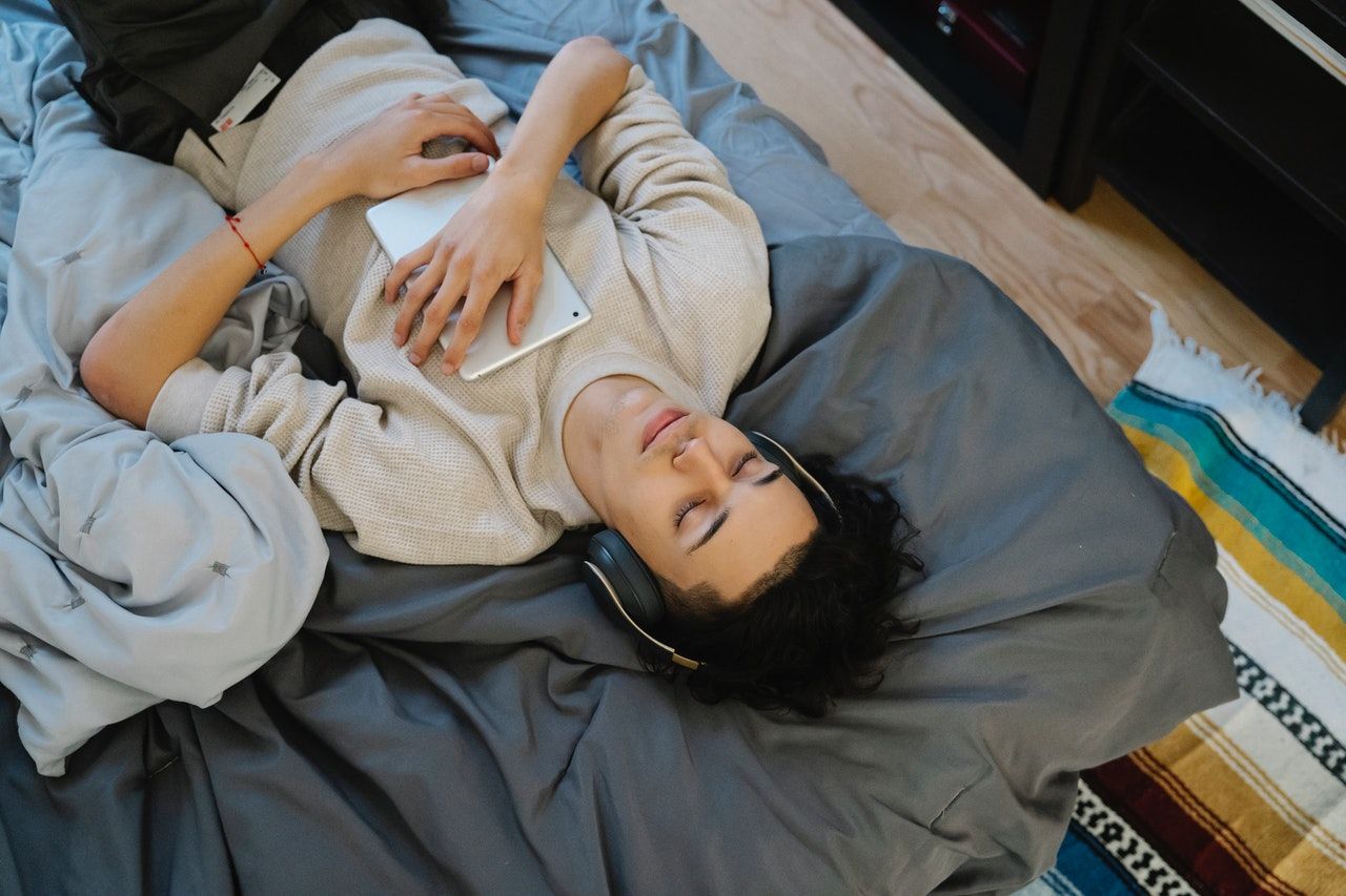 Image shows a person lying on a bed with headphones on listening to music