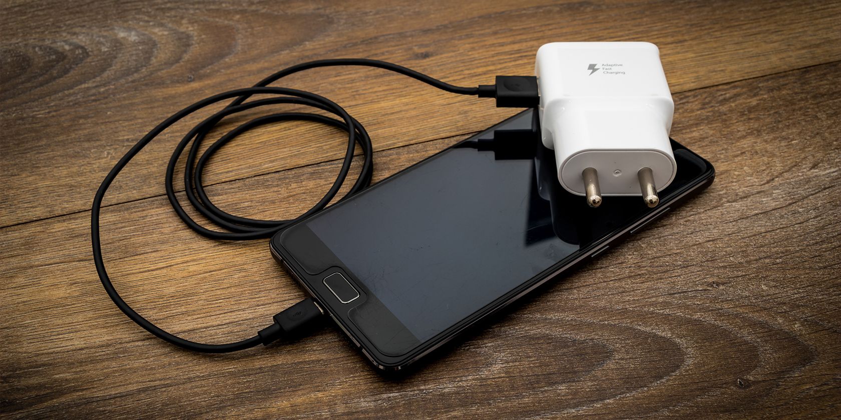 a smartphone, charger, and cable on a desk