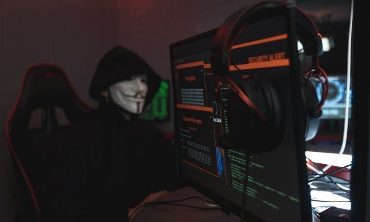 person in anonymous costume at computer with security alert on it