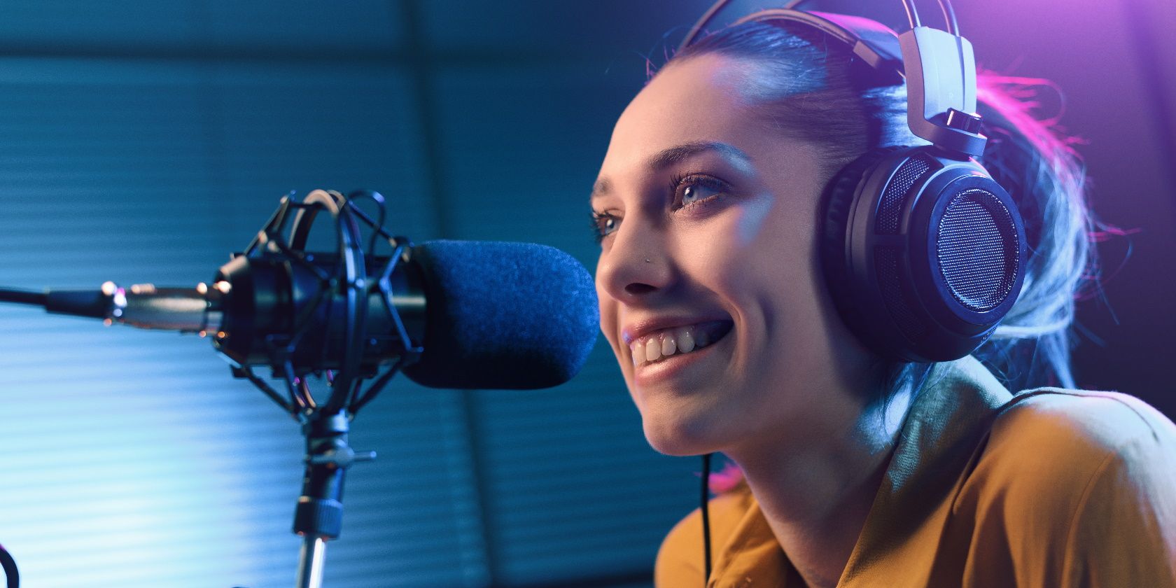 Young smiling woman wearing headphones and speaking into a microphone at the radio station, entertainment and communication concept