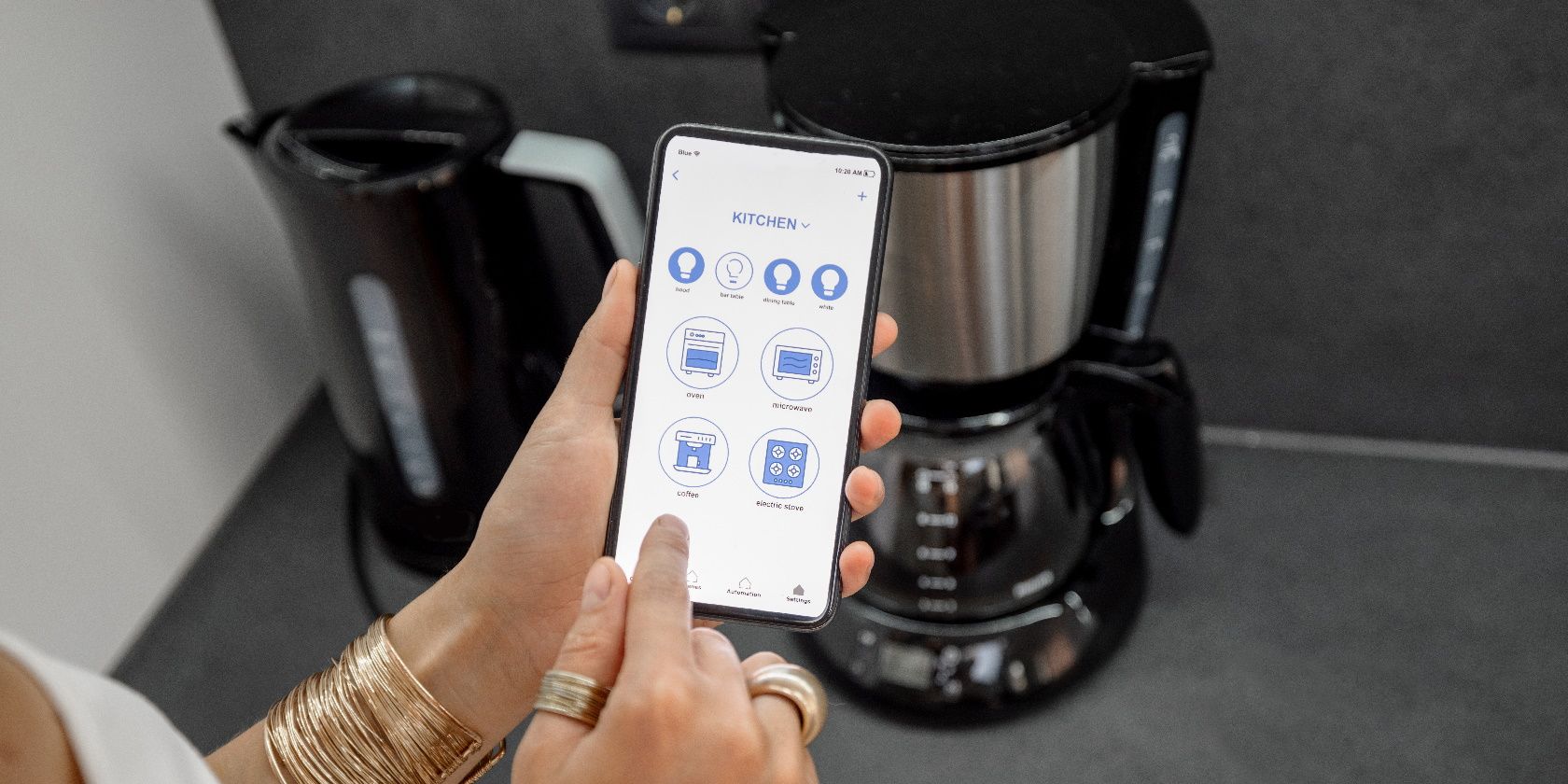 Smartphone with current mobile application to control smart devices in the kitchen.  Female control coffee machine or electric teapot with home phone.  Smart home concept