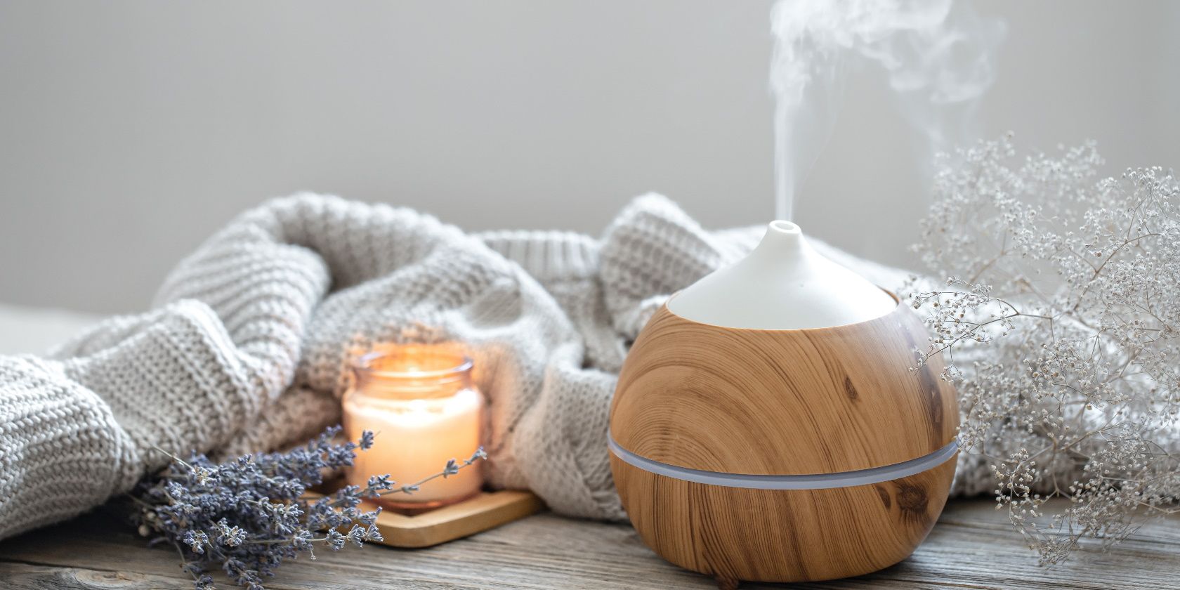 Aroma composition with a modern aroma oil diffuser on a wooden surface with a knitted element, candle and lavender.