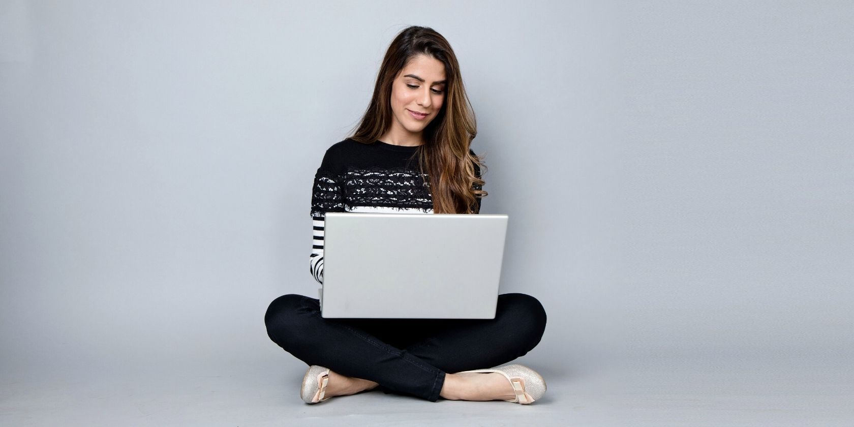 A girl typing on a laptop while leaning on a wall