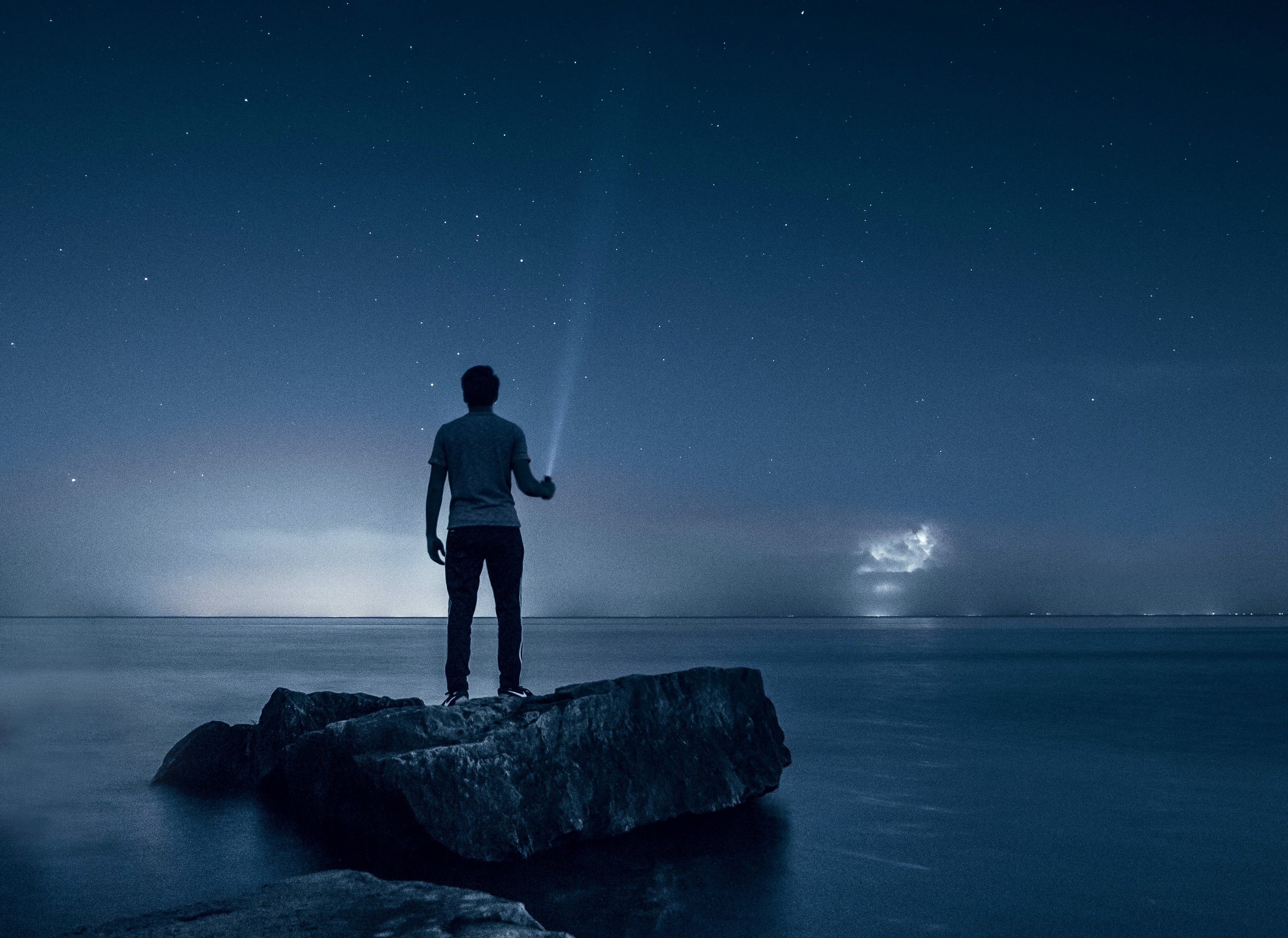 A person on a rock in the middle of the ocean at night.