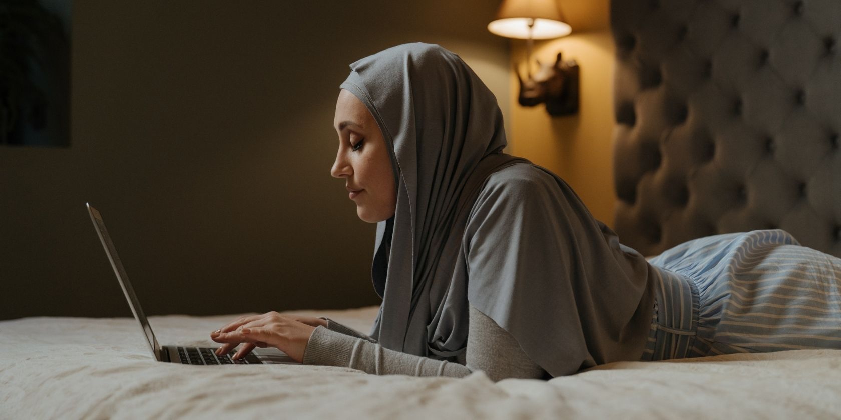 Woman in hijab on bed with laptop