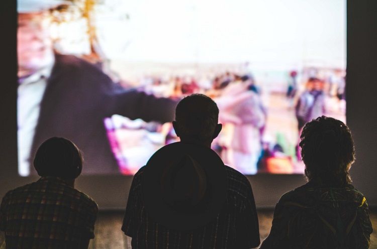 three people watching a movie on a large screen