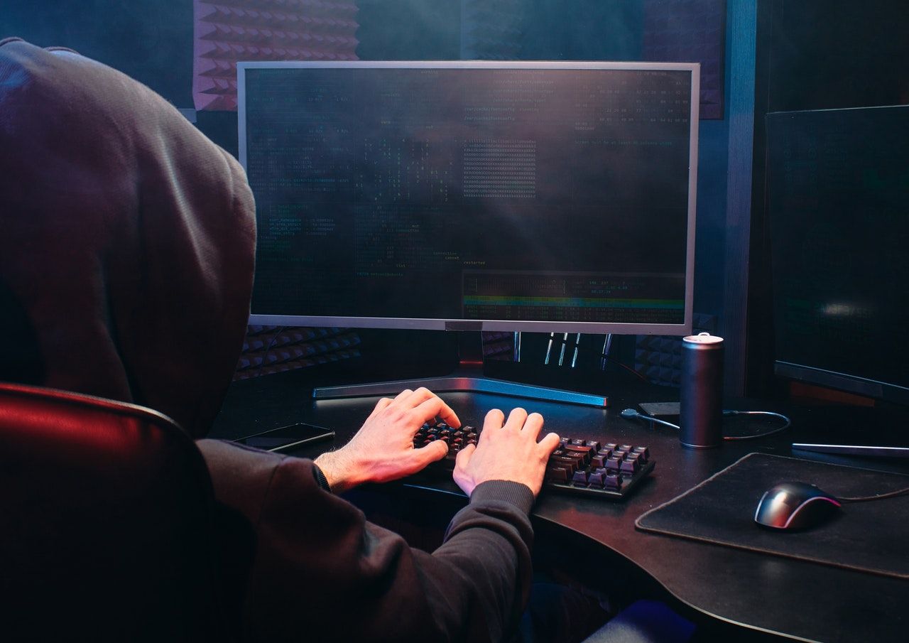 Person with a hoodie sitting in front of a computer in a dimly lit place 