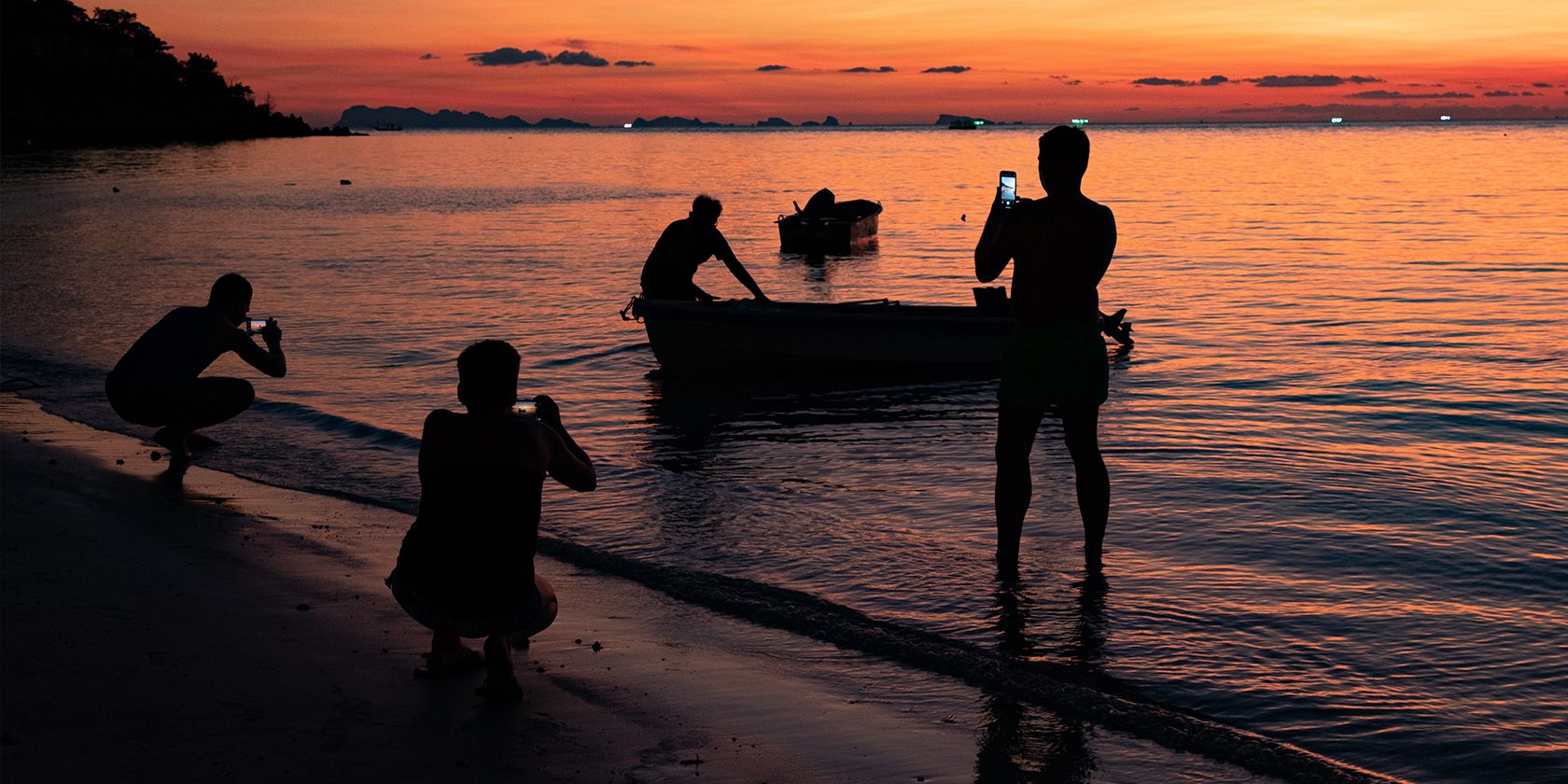 three people taking sunset images on a beach with a fisherman on the foreground