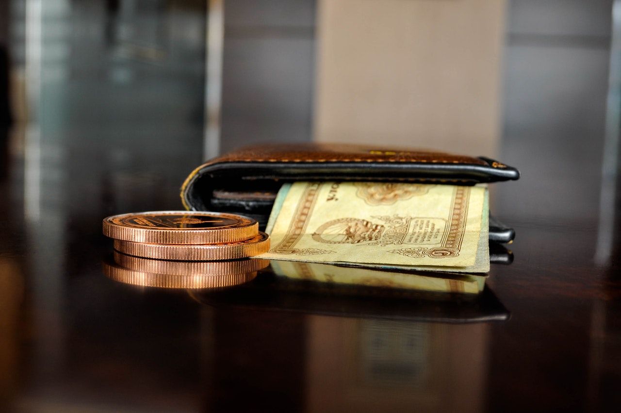 Brown leather bifold wallet resting on a table with money notes and a coin