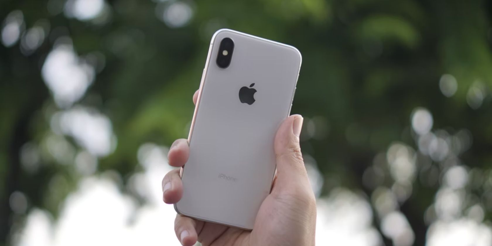 hand holding silver iphone x against background of trees 