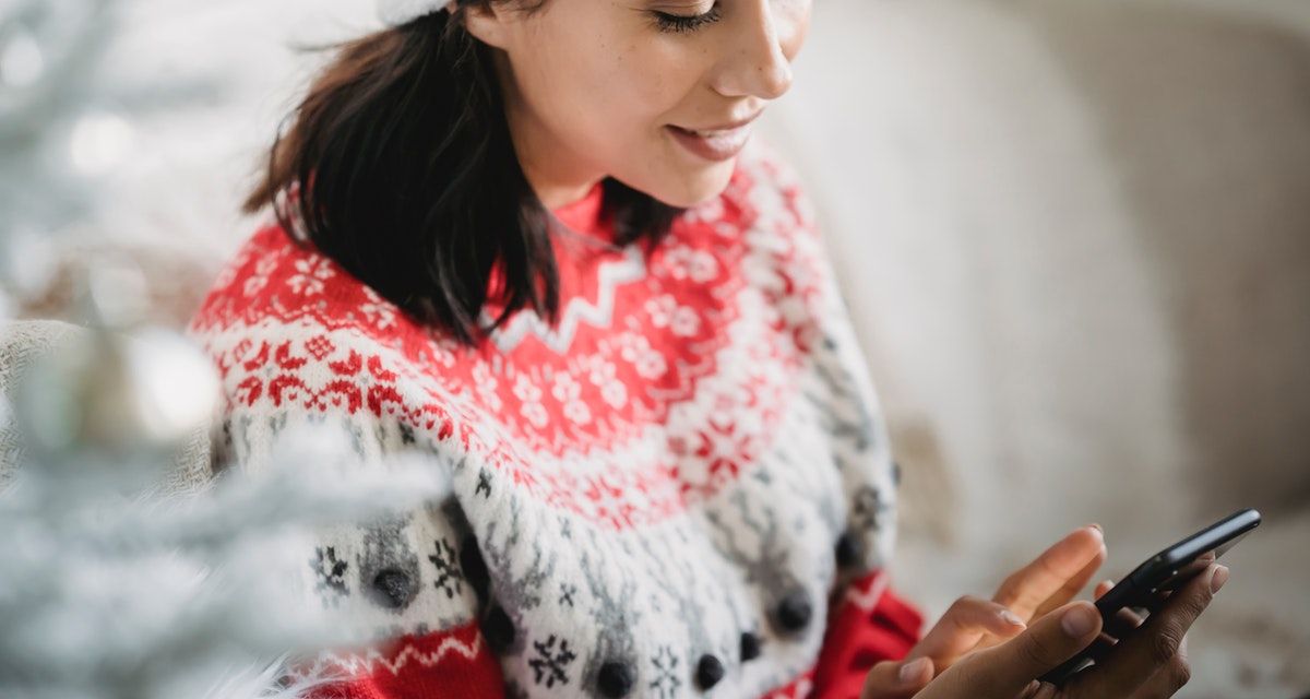 wanita dengan sweter natal memegang telepon