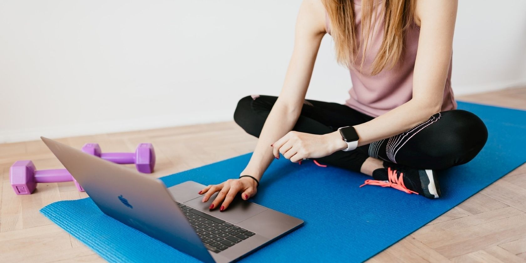 A woman sitting on a fitness mat with her laptop