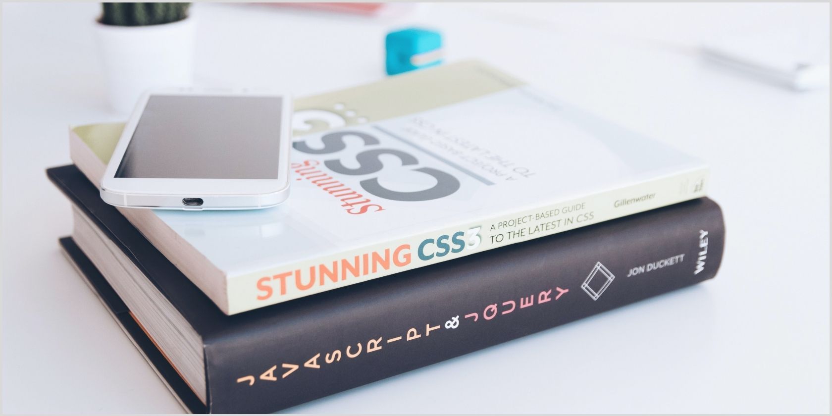 A book titled “Stunning CSS” lies on top of a book on JavaScript. A mobile phone lies on top of both.